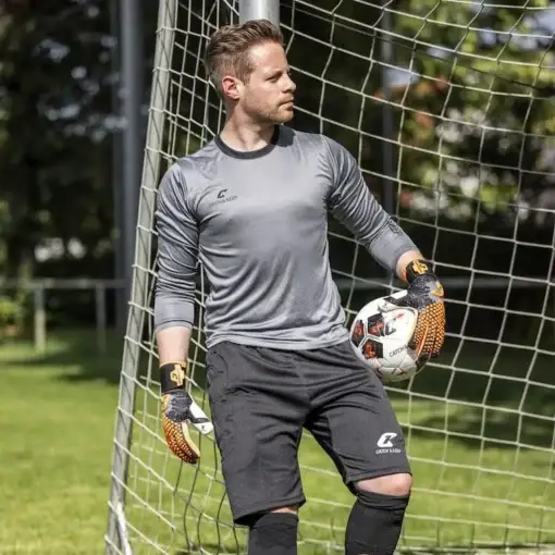 Herren Torhüter mit kurzer Torwarthose von Catch and Keep steht im Tor und hölt einen Fussball in der linken Hand