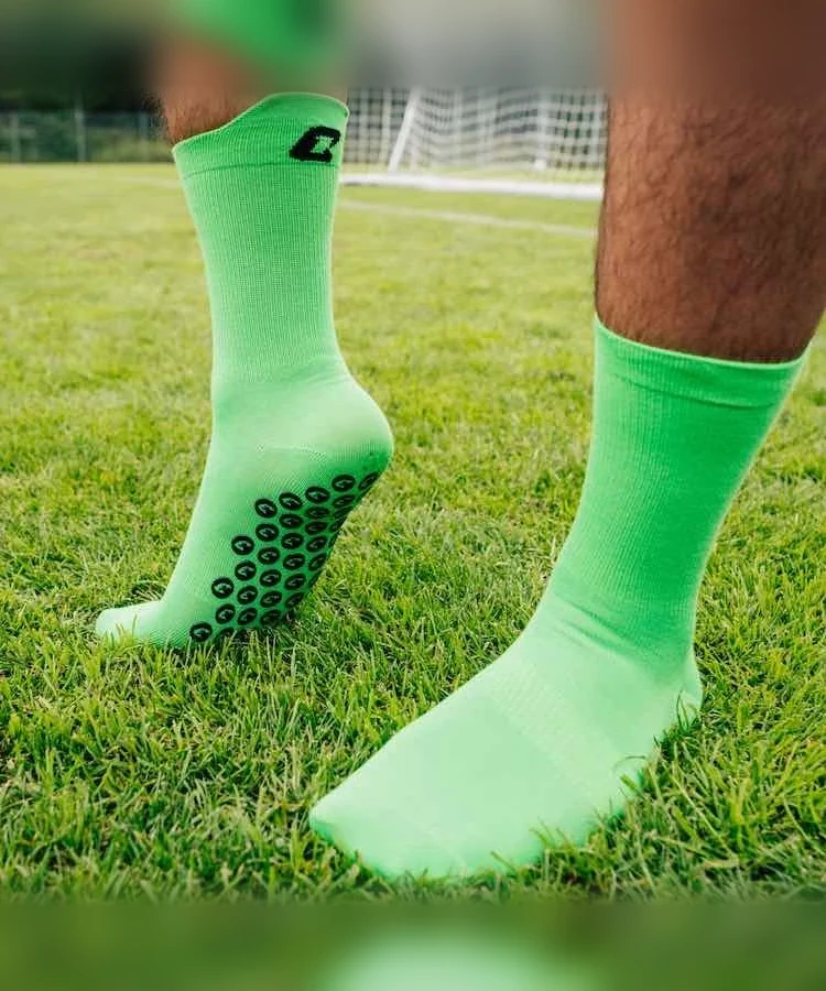Performance Grip Socke in Grün getragen auf dem Rasen – Grip-Elemente an der Sohle sichtbar