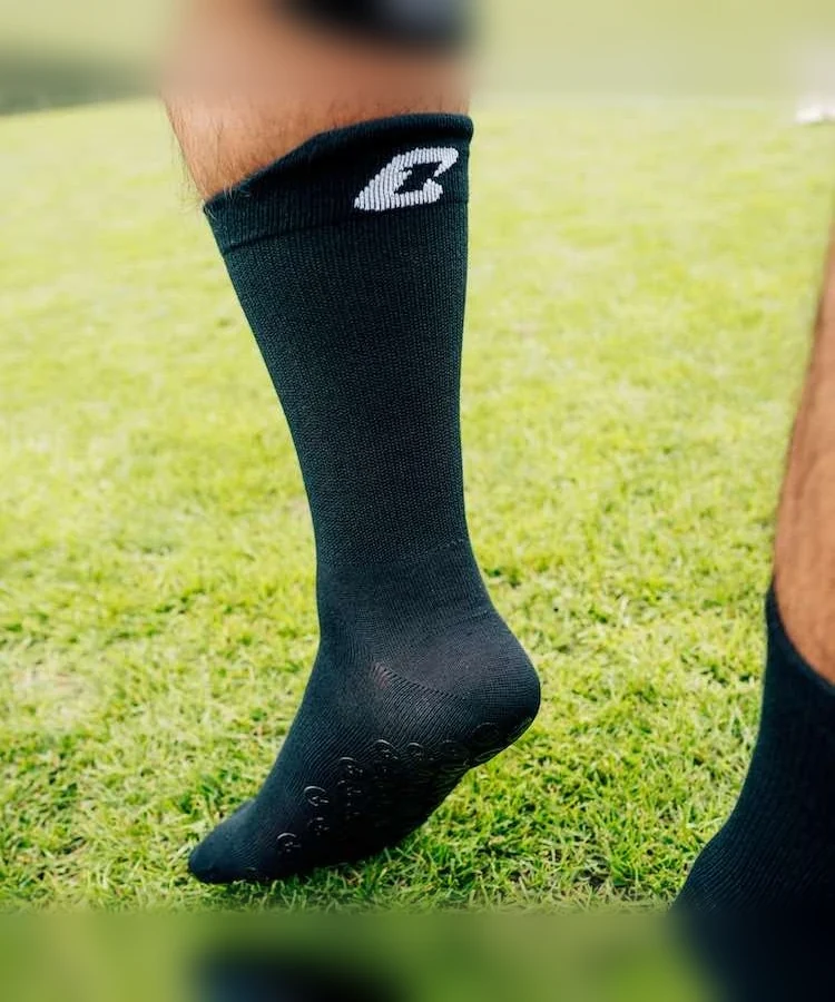Performance Grip Socke in Schwarz getragen auf dem Rasen – Grip-Elemente an der Sohle sichtbar