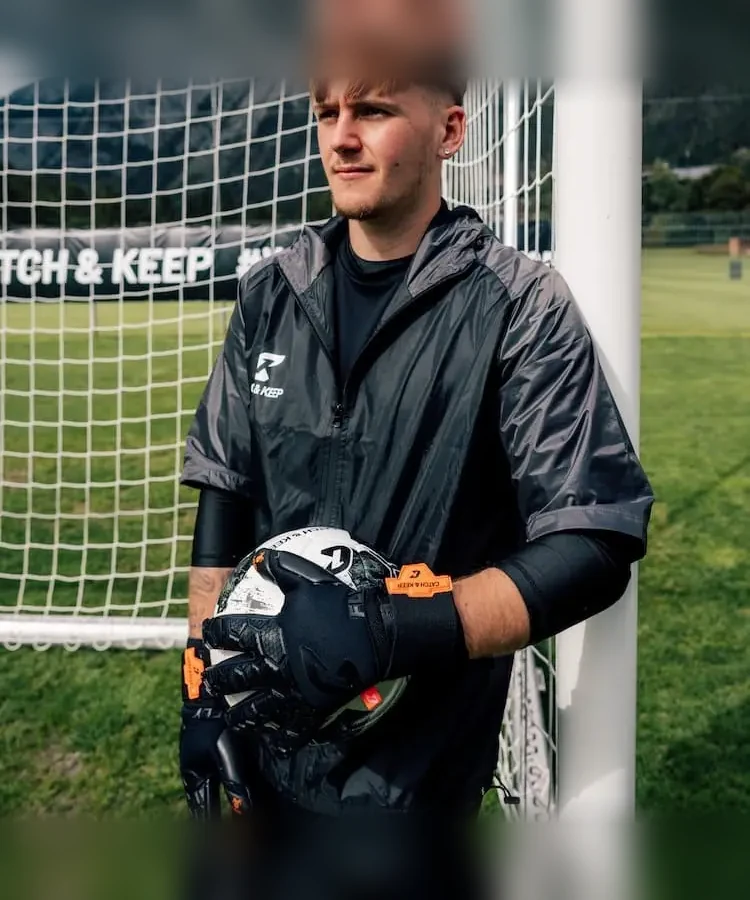Torwart in schwarzer Jacke hält den Ball mit schwarzen Fly Soul Torwarthandschuhen