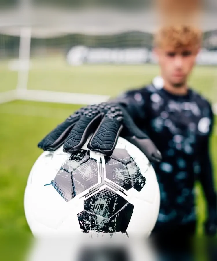 Hand im schwarzen Nero Torwarthandschuh liegt auf dem Ball
