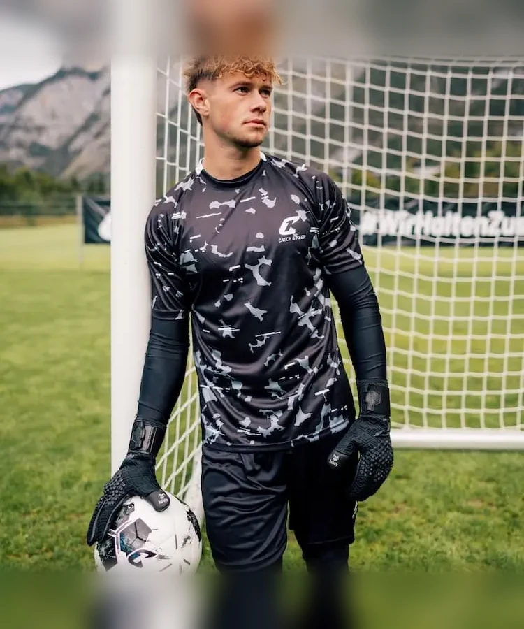 Torwart steht mit Ball und schwarzen Nero Torwarthandschuhen am Pfosten