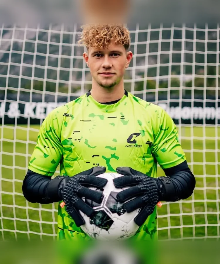 Torwart im grünen Trikot hält den Ball mit schwarzen Nero Torwarthandschuhen